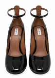 A pair of black patent leather heel pumps with ankle straps, shown from a top-down view on a white background. The brand name ALAIA is visible on the insole.