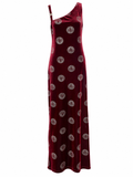 A one-shoulder velvet maxi dress in deep burgundy red, featuring a repeating circular gold and silver pattern, shown against a plain white background.
