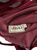 Close-up of a Versace Intensive garment label sewn onto a burgundy satin and velvet fabric, with a Greek key pattern visible on the velvet trim.