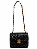 A black quilted patent leather shoulder bag with a gold-tone interlocking CC logo on the front, featuring a gold chain and black leather shoulder strap, set against a plain white background.