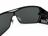 Close-up of a pair of black rimless sunglasses with dark lenses, showing the temple arm with a white 'toi' logo and silver hinge details on a white background.