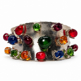 A wide silver cuff bracelet decorated with multiple colorful faceted gemstones in red, green, blue, orange, and purple, set against a plain white background.