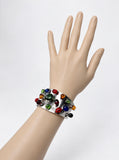 A wide Gucci silver cuff bracelet decorated with multiple colorful glass beads, displayed on a beige mannequin hand against a light gray background.