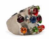 A wide silver cuff bracelet featuring multiple colorful round cabochon gemstones in red, blue, green, orange, and dark red, set against a plain white background.