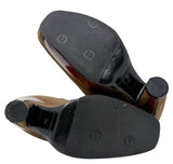 A pair of women's high-heeled shoes shown from the sole, featuring black textured non-slip grip pads and black rubber heel caps, with a brown patent leather heel and a beige insole visible.