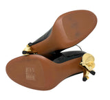Black patent leather ALAIA heels with sculptural gold metal flower details on the heels, shown from a top-down view on a white background.