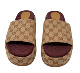 A pair of Gucci slide sandals featuring the signature GG monogram canvas in beige and brown, with a burgundy insole, shown against a plain white background.