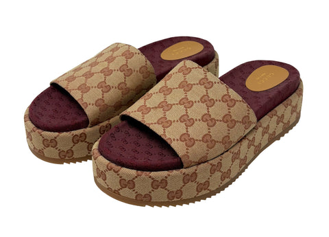 A pair of Gucci platform slide sandals featuring the brand's classic GG monogram canvas in beige and brown, paired with a deep burgundy mesh footbed and a thick brown platform sole.