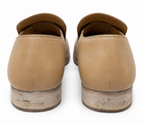 A pair of tan leather slip-on loafers shown from the back, featuring a low stacked wooden heel and a distressed finish.