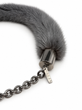 A close-up of a dark gray faux fur collar with a silver-toned metal cap and chain, featuring a small engraved brand tag on the clasp.