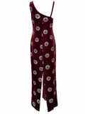 A one-shoulder velvet jumpsuit in deep burgundy with a repeating circular silver and white pattern, shown against a plain white background.