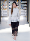Person wearing a white pinstripe blouse and black lace pants in a futuristic setting.
