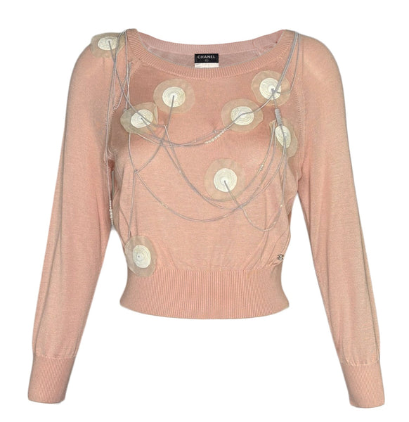 A pale pink long Chanel sleeve knit top with circular metallic embellishments and draped chain details on the front, shown against a plain white background.