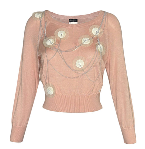 A pale pink long Chanel sleeve knit top with circular metallic embellishments and draped chain details on the front, shown against a plain white background.