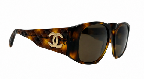 Chanel sunglasses with a brown and black tortoiseshell pattern, featuring a woven leather detail on the temple and a gold-tone interlocking CC logo.