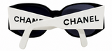Chanel sunglasses with a bold white front band featuring the black CHANEL logo, black frames, and dark lenses, shown on a plain white background.