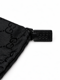 Close-up of a black Gucci nylon pouch with the embossed GG logo and a black leather tab stamped with 'GUCCI DOG' on a white background.